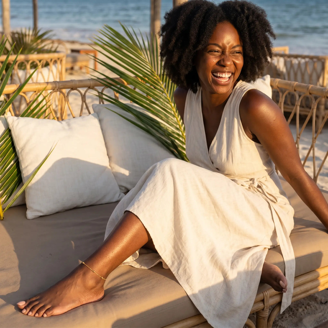A joyful woman wearing a linen dress and Beaded Station Anklet, enjoying beach vibes by the ocean, from Brother & Sisters.