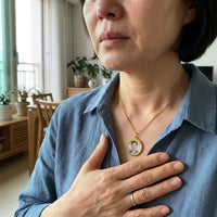 Thumbnail for Woman moved to tears, her hand on the gold round photo necklace holding a late loved one's photo | SKU: TPH-RNDN-GOLD